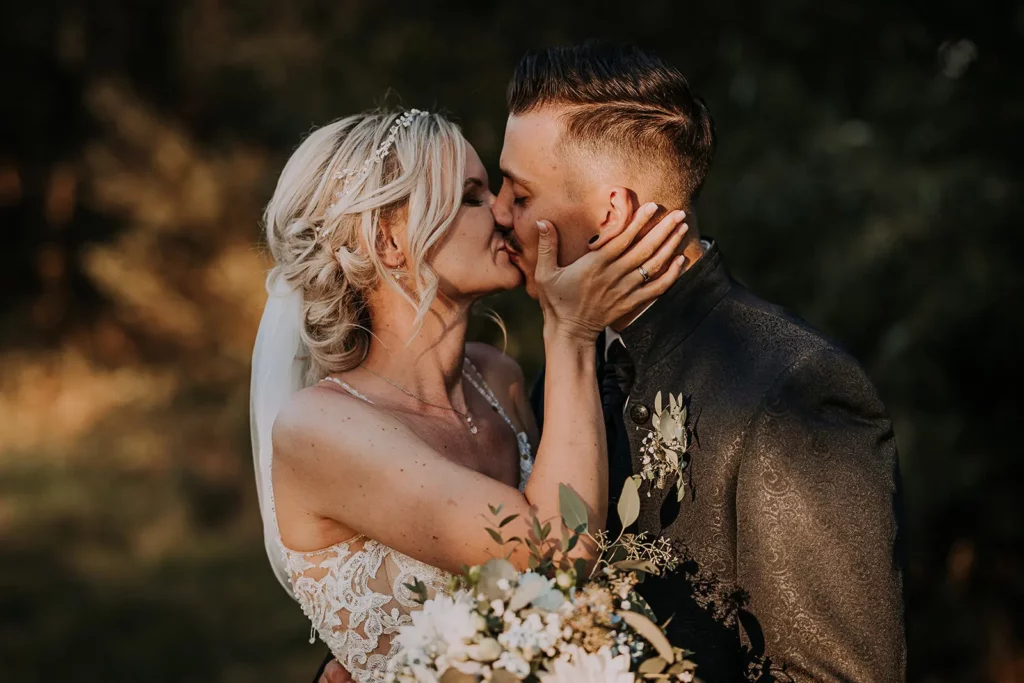 Braut und Bräutigam küssen sich innig, Braut hält einen Blumenstrauß, fotografiert von einer Hochzeitsfotografin in der Hochzeitsscheune Redwitz.